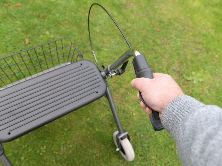 Ein Rollator auf einer grünen Wiese, an dem sich eine Person festhält.