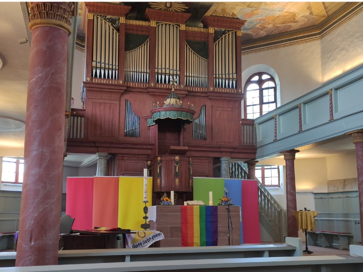 In der Kirche in Groß-Rohrheim sind Orgel und Altar mit Tüchern in Regenbogenfarben geschmückt.