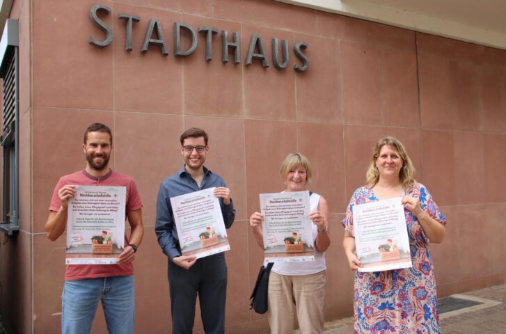 Vor dem Stadthaus in Lampertheim stehen zwei Männer und zwei Frauen, die je ein Plakat zur Kamera halten. Dieses Plakat lädt zur Informationsveranstaltung am 3. September ein.