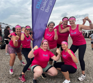 Das Team Rimbach, 7 Frauen der Regionalen Diakonie Bergstraße stehen in Siegespose zum Gruppenfoto zusammen. Im Hintergrund die lila Beach-Flag der Regionalen Diakonie Bergstraße